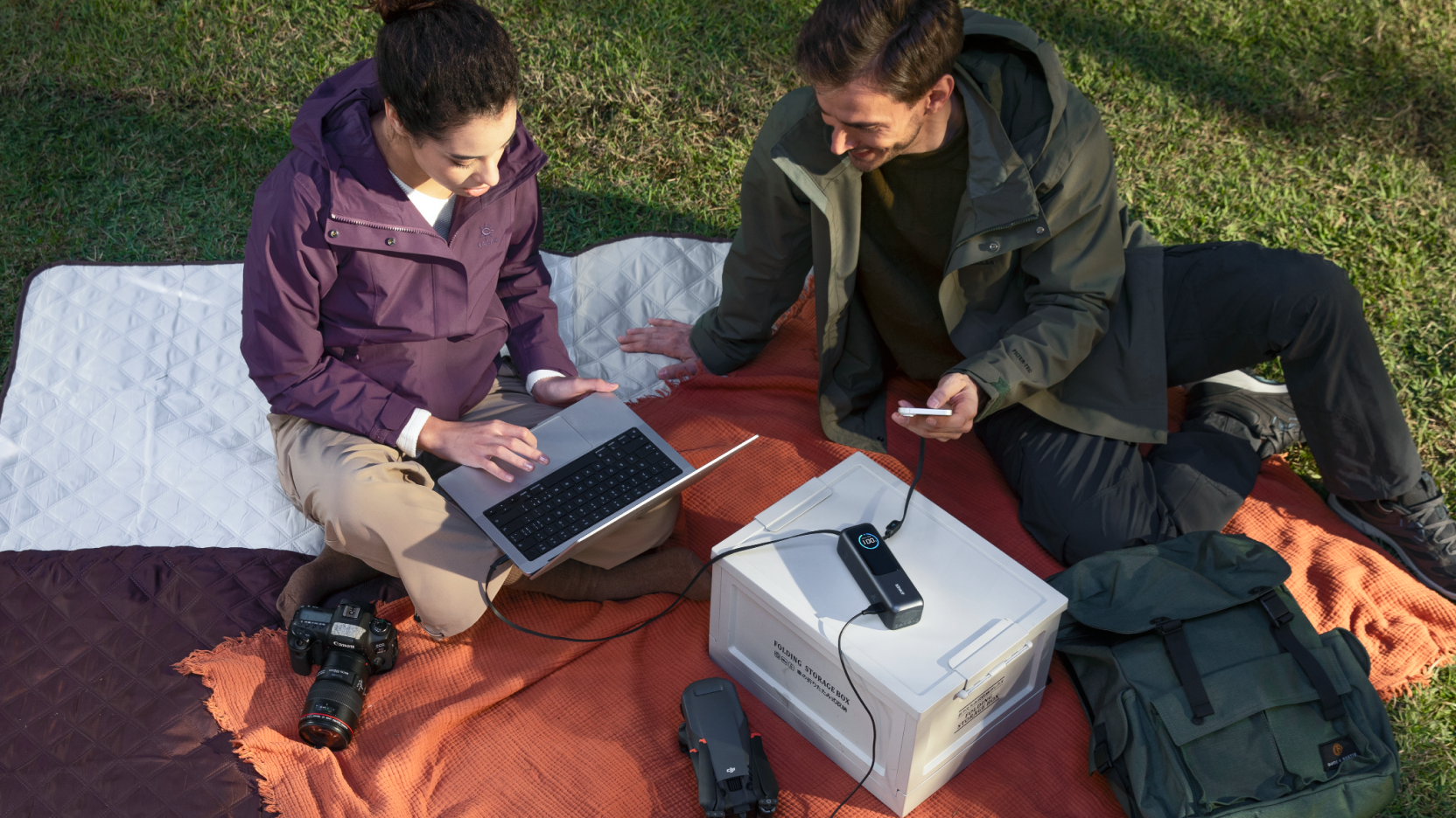 Two people using the Anker 25K Power Bank outdoors, charging a laptop and smartphone simultaneously, showcasing its high-capacity USB-C fast charging for travel and work.