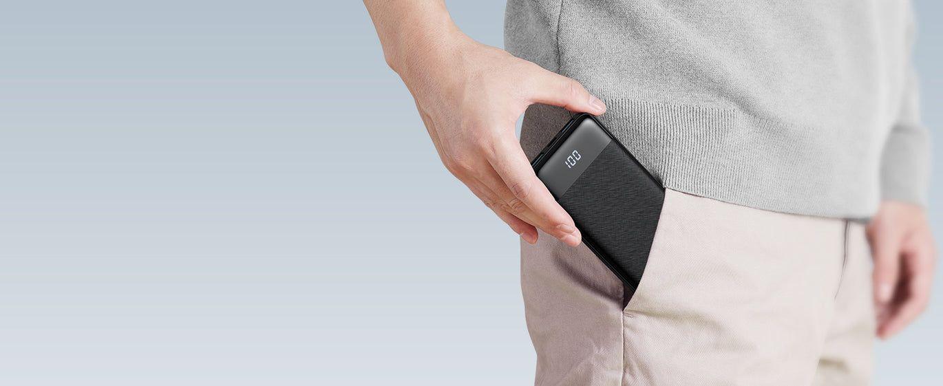 Person placing a slim black power bank with digital battery display into their pocket, demonstrating its compact and portable design.